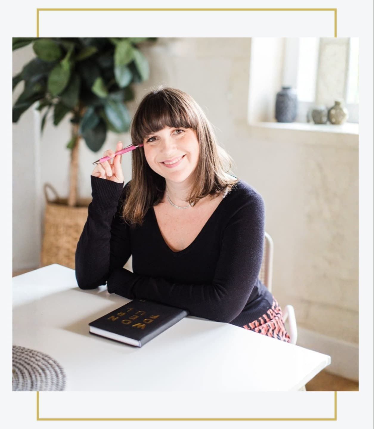 Tara Rule sitting at a desk with a notebook and pen, smiling in her workspace.