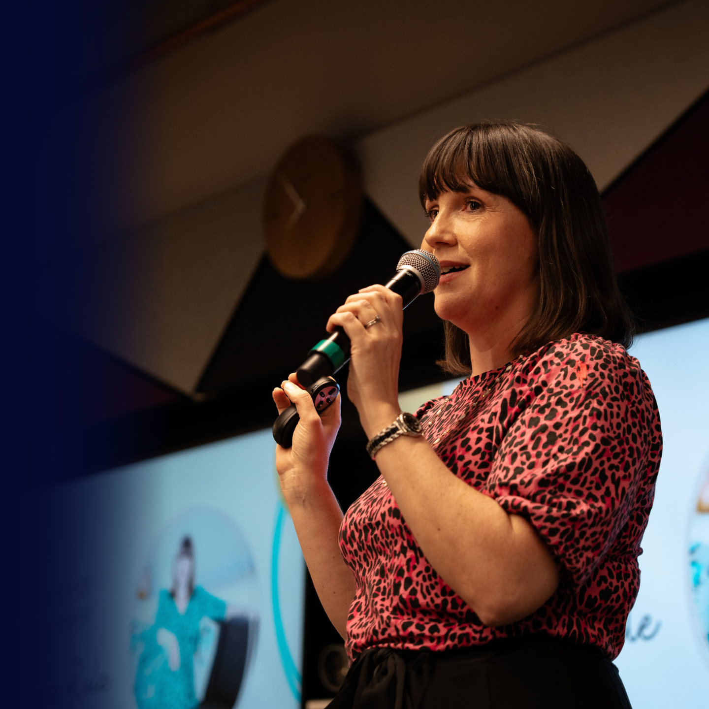 Tara Rule speaking on stage, holding a microphone and presenting to an audience during a leadership development event.