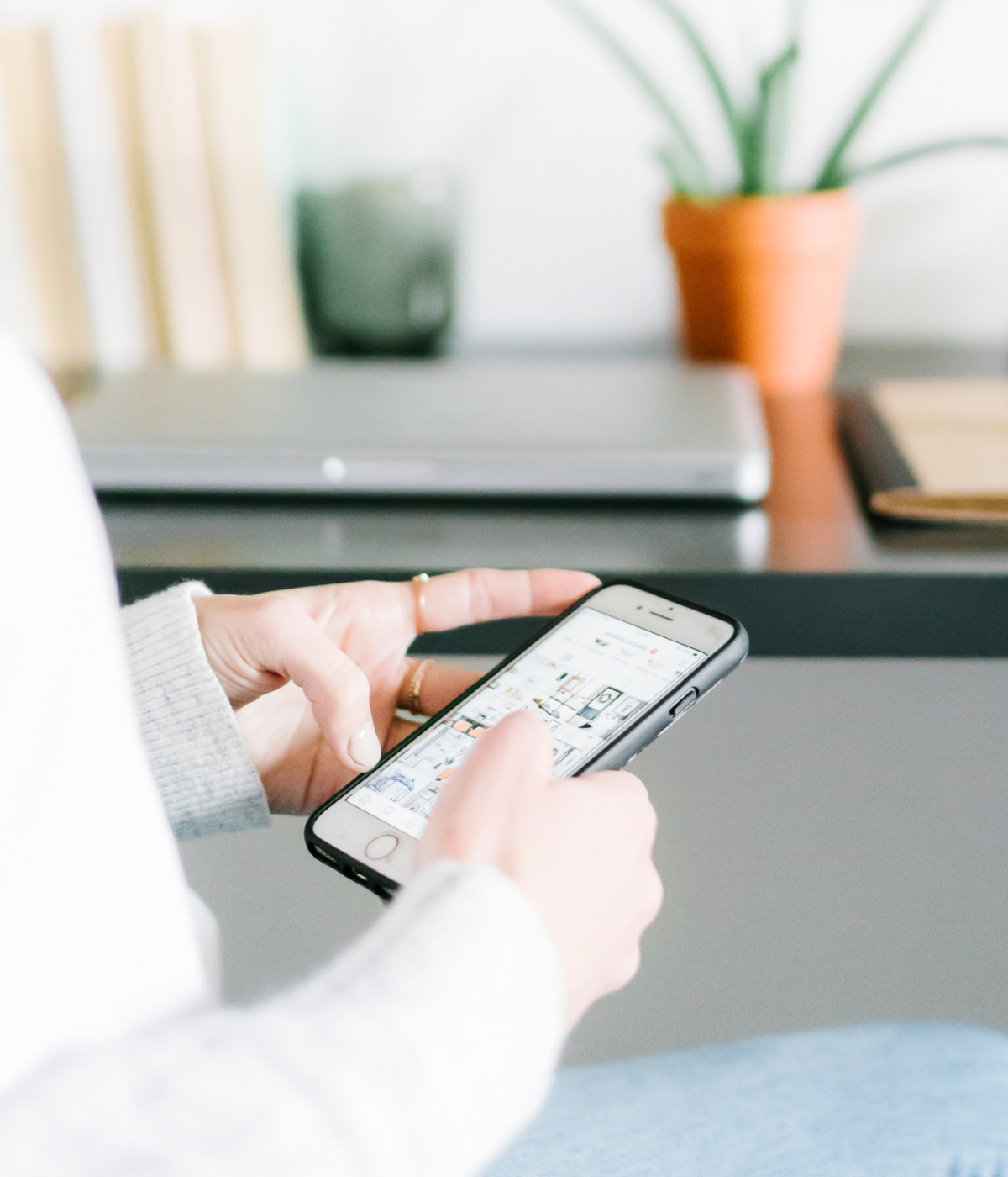 woman scrolling on phone with computer in background