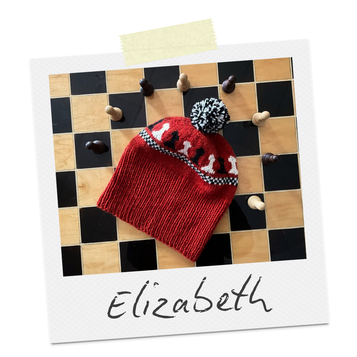 Polaroid with the word Elizabeth written on it. The photo shows a red hat with a chess themed colourwork design and black and white pom pom. It is displayed on a chessboard surrounded by chess pieces