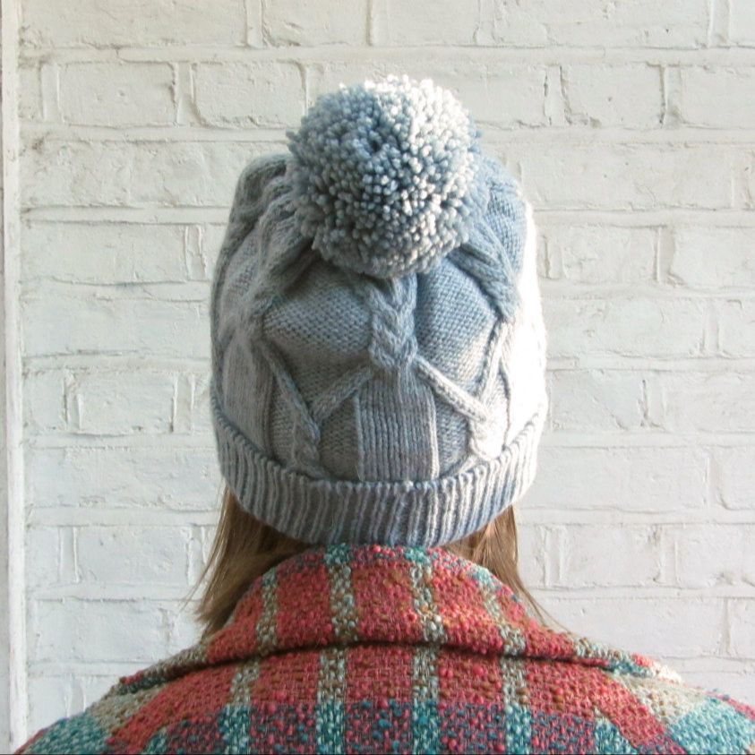 Back view of a pale blue cabled hat with a large pom pom