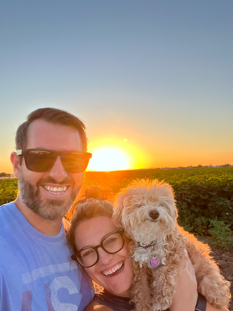 Chelsey, her husband and their dog Chloe smiling at sunset
