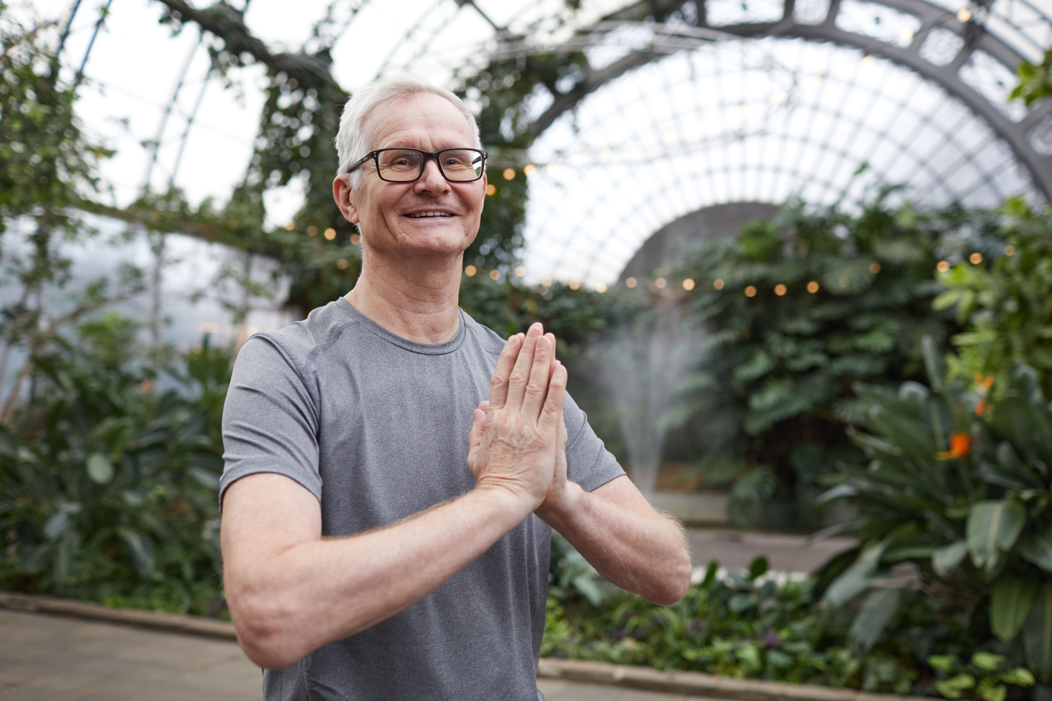 Man meditates in greenhouse with prayer hands.