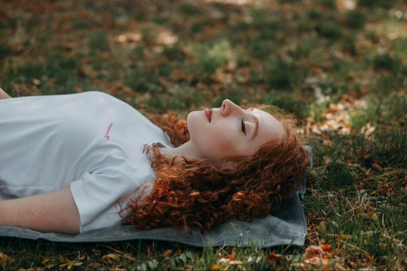 Woman meditates on yoga mat laying down in the grass.