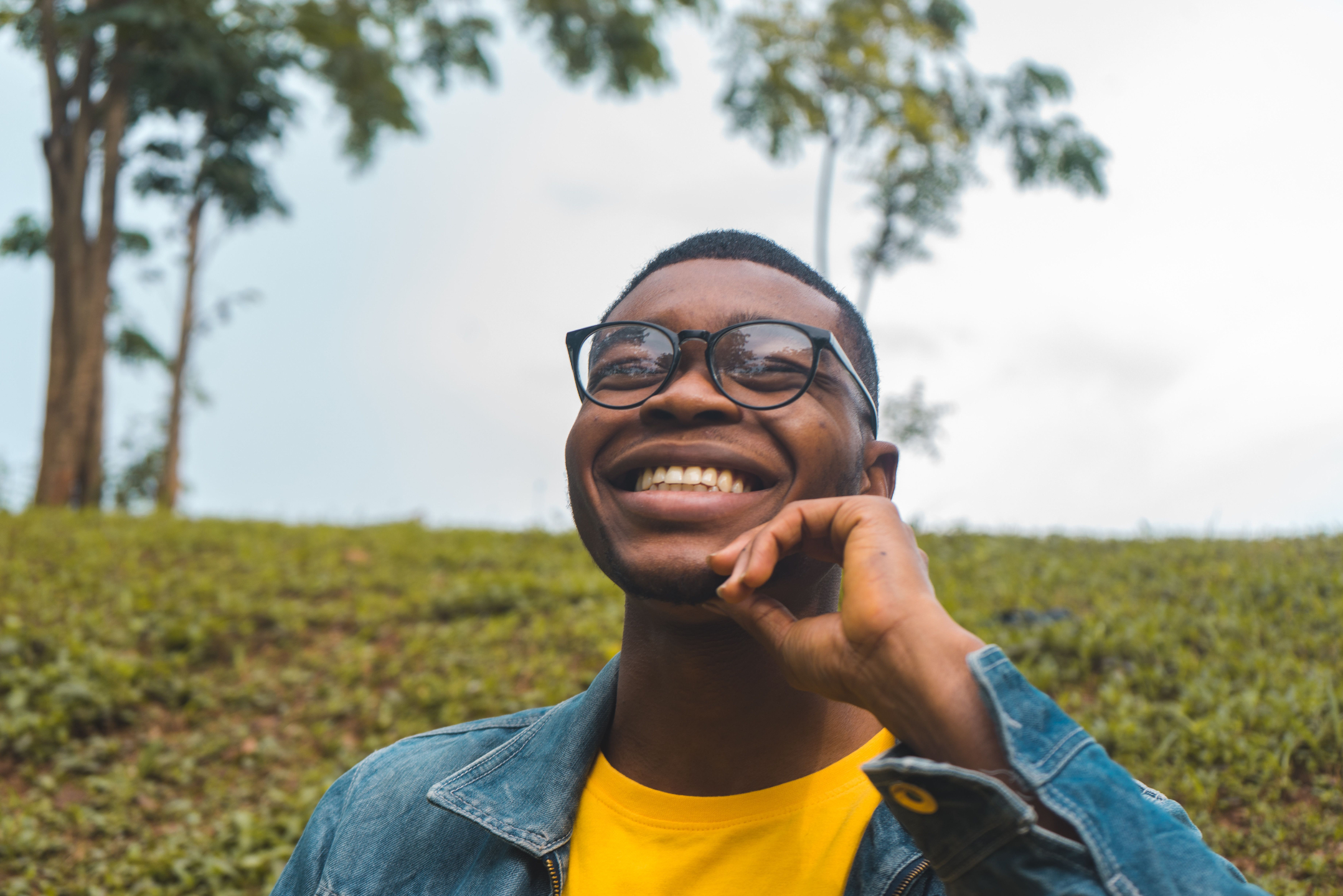 Young man with glasses smiles outside in a field of grass.