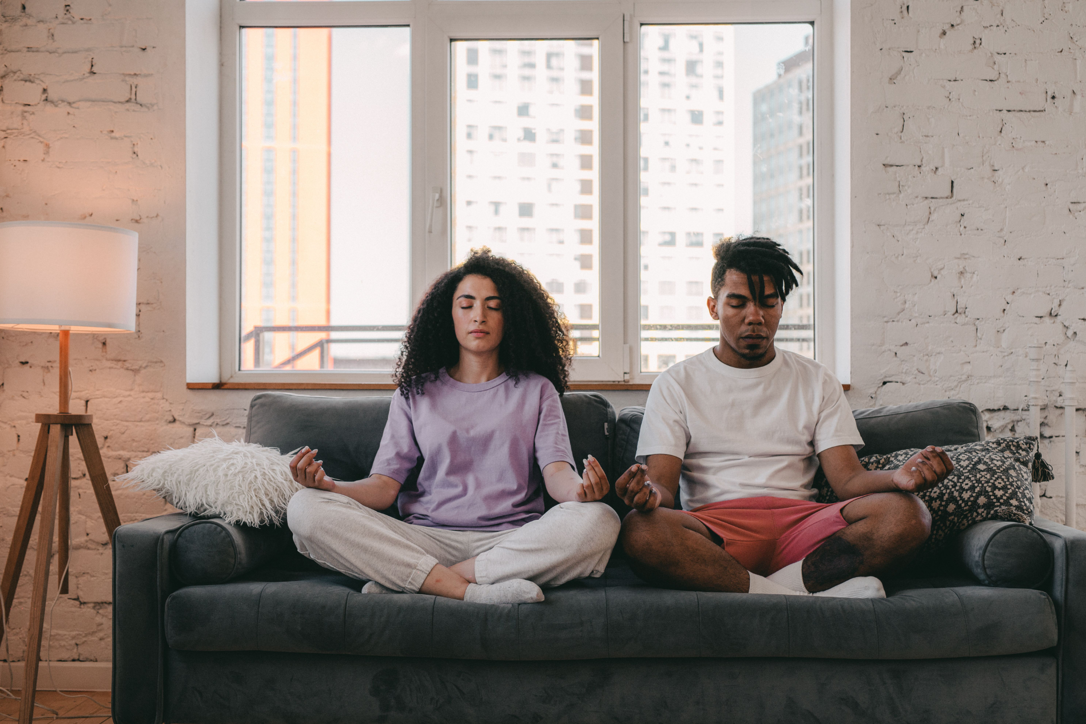 Two young adults sit in meditation on the couch.