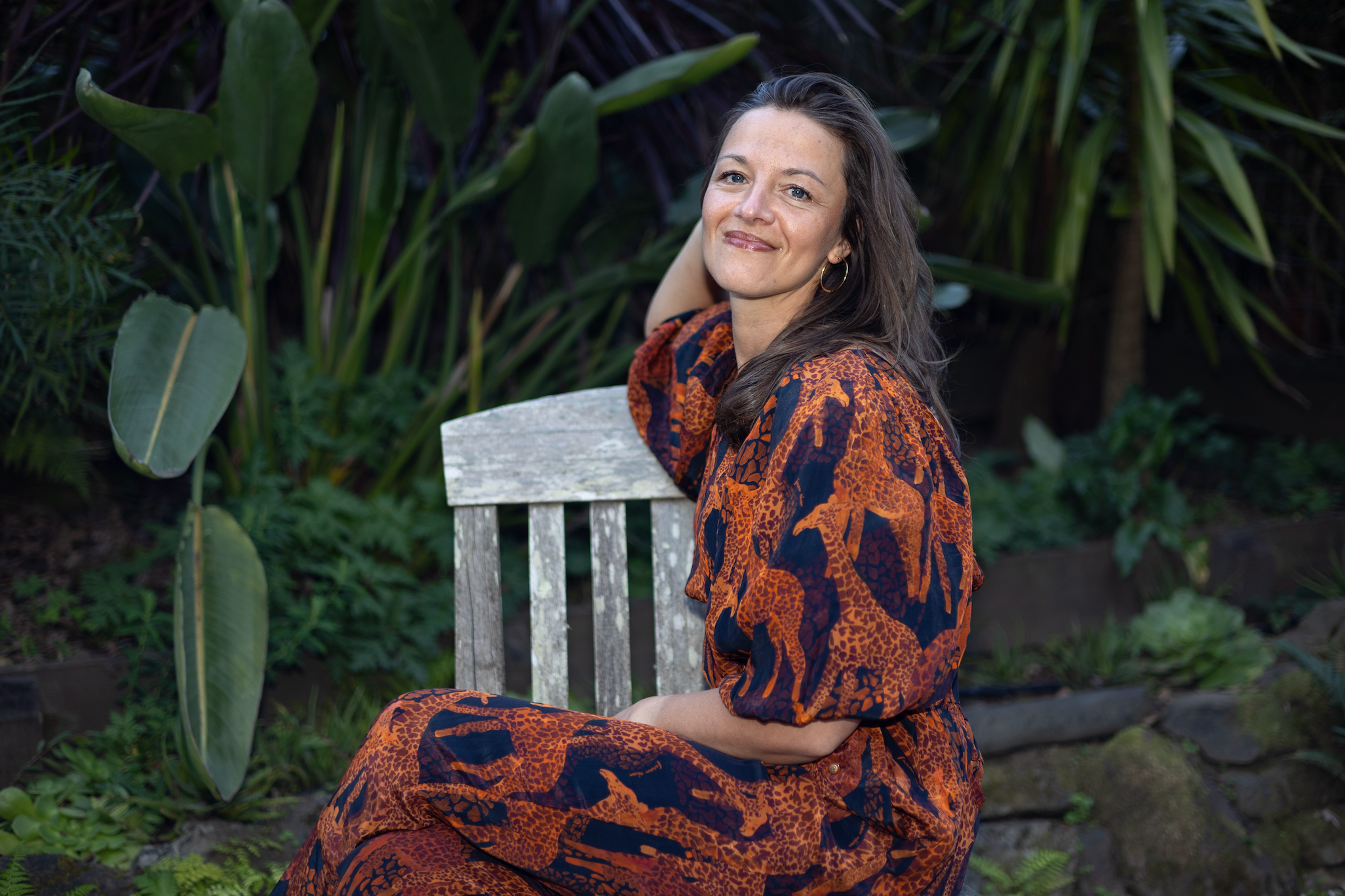 Steffi Seefeld seated outdoors on a garden bench, smiling warmly — somatic trauma-informed coach