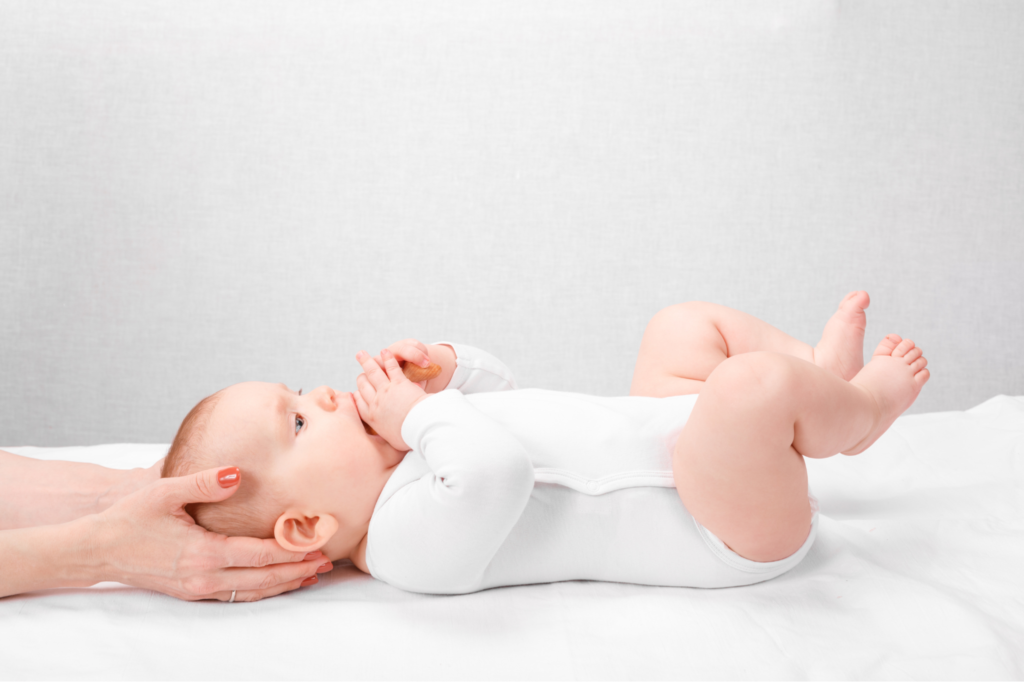 Mother gently holding baby’s head to support positioning for plagiocephaly and torticollis management.
