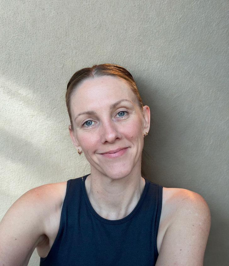 Alison Balson wears a brown shirt, resting on a white couch with her head rested against her left arm