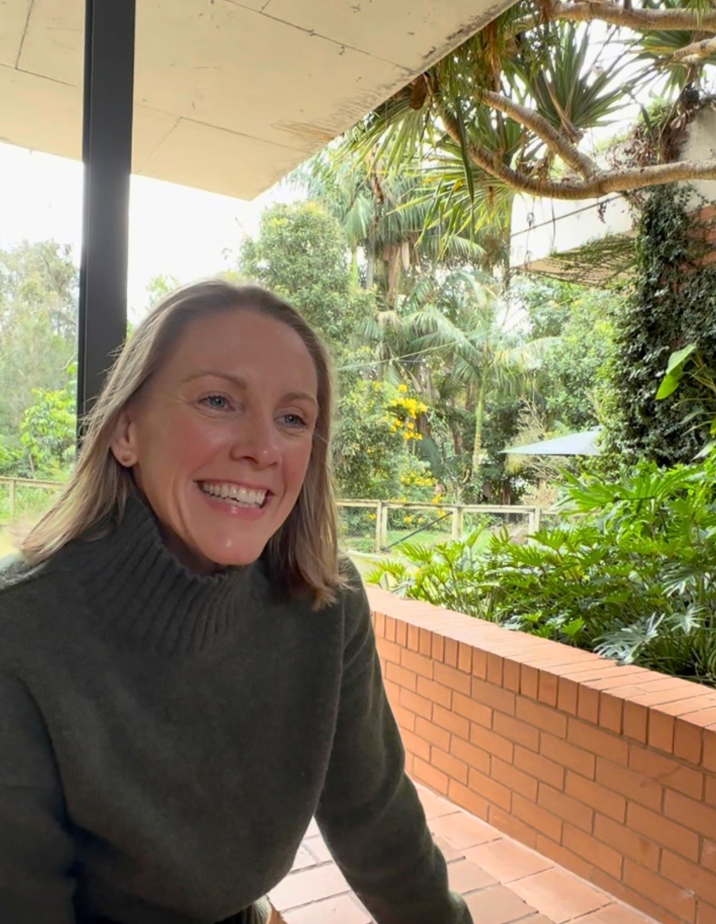 Alison Balson sits at bar stool in white kitchen smiling at the camera