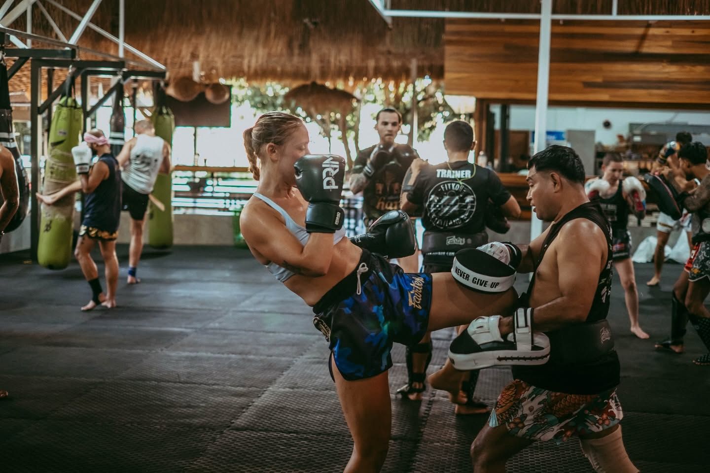 Guest landing a kick on the pads held by a Thai coach