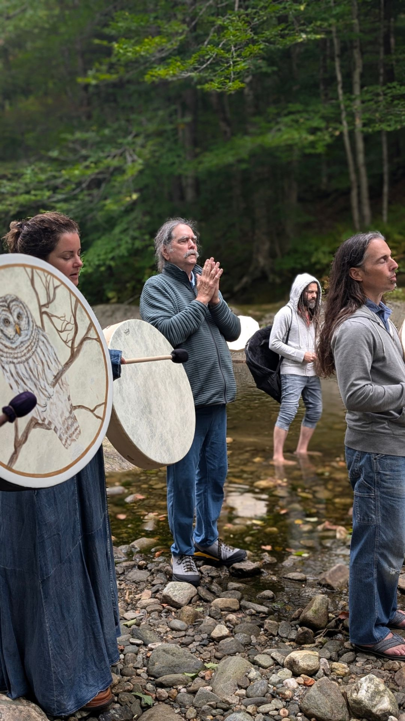 people with native american drums standing devotional in a river bed
