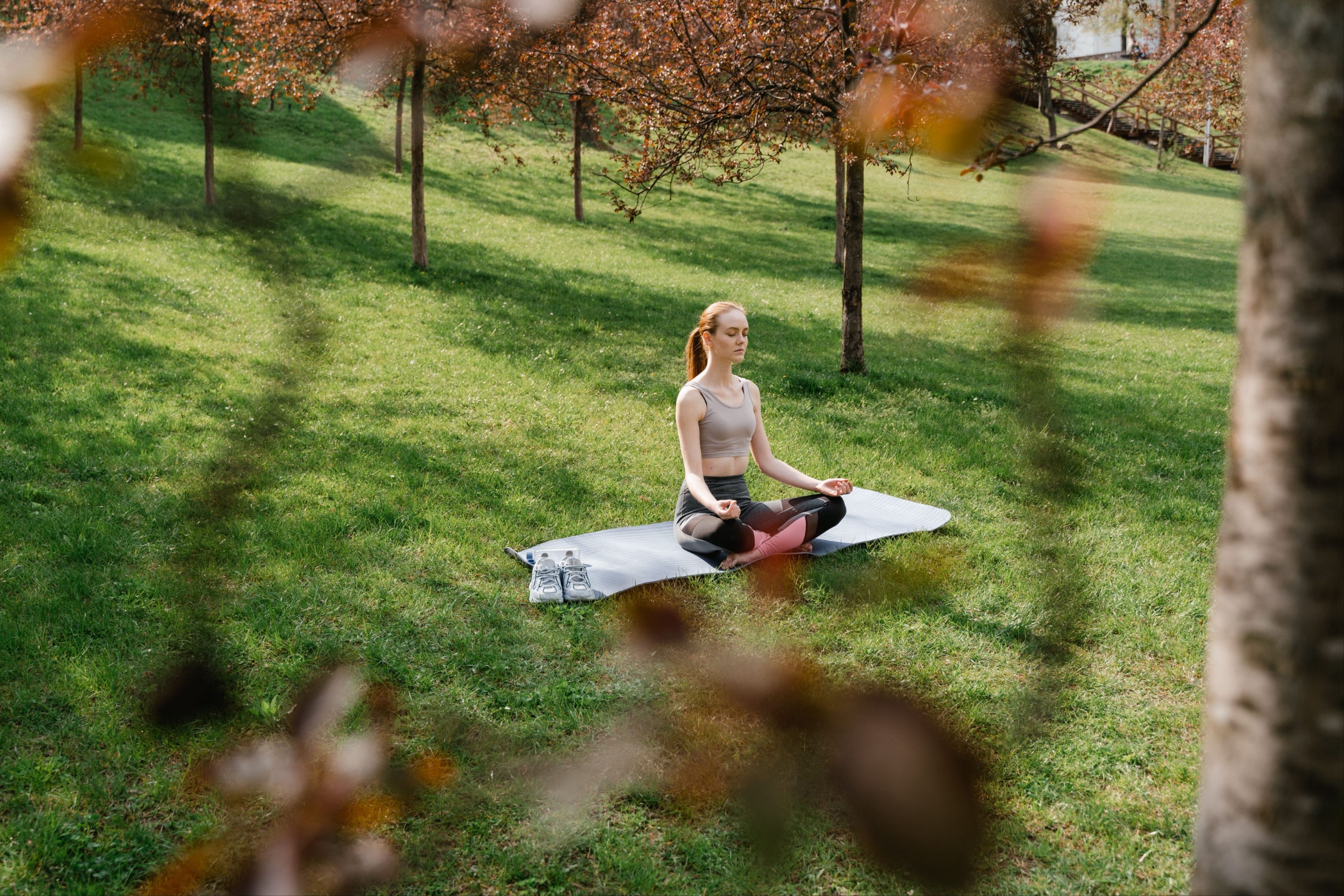 Young woman sits in a beautiful park and meditates on her yoga mat.