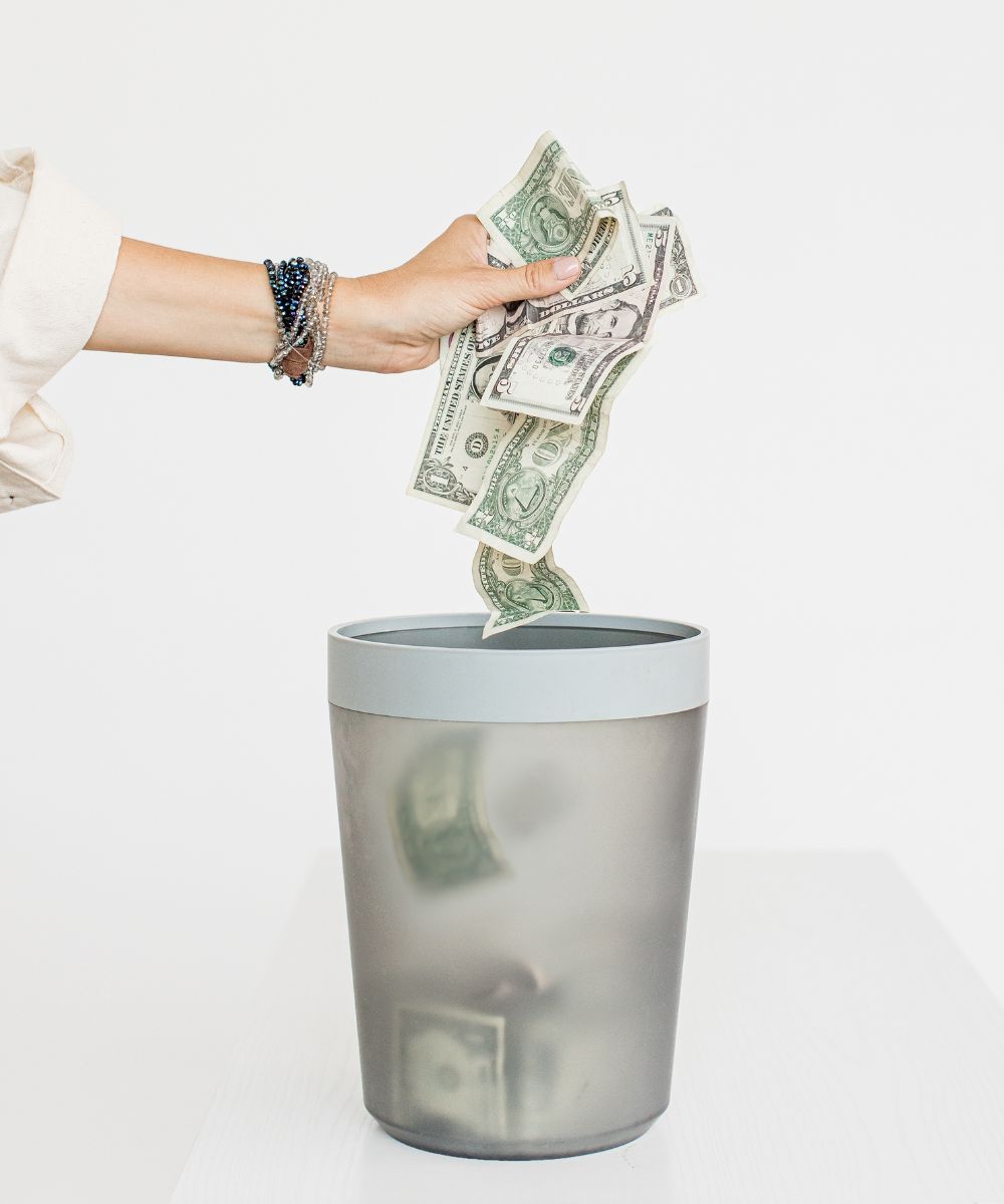hand throwing money into a trash can