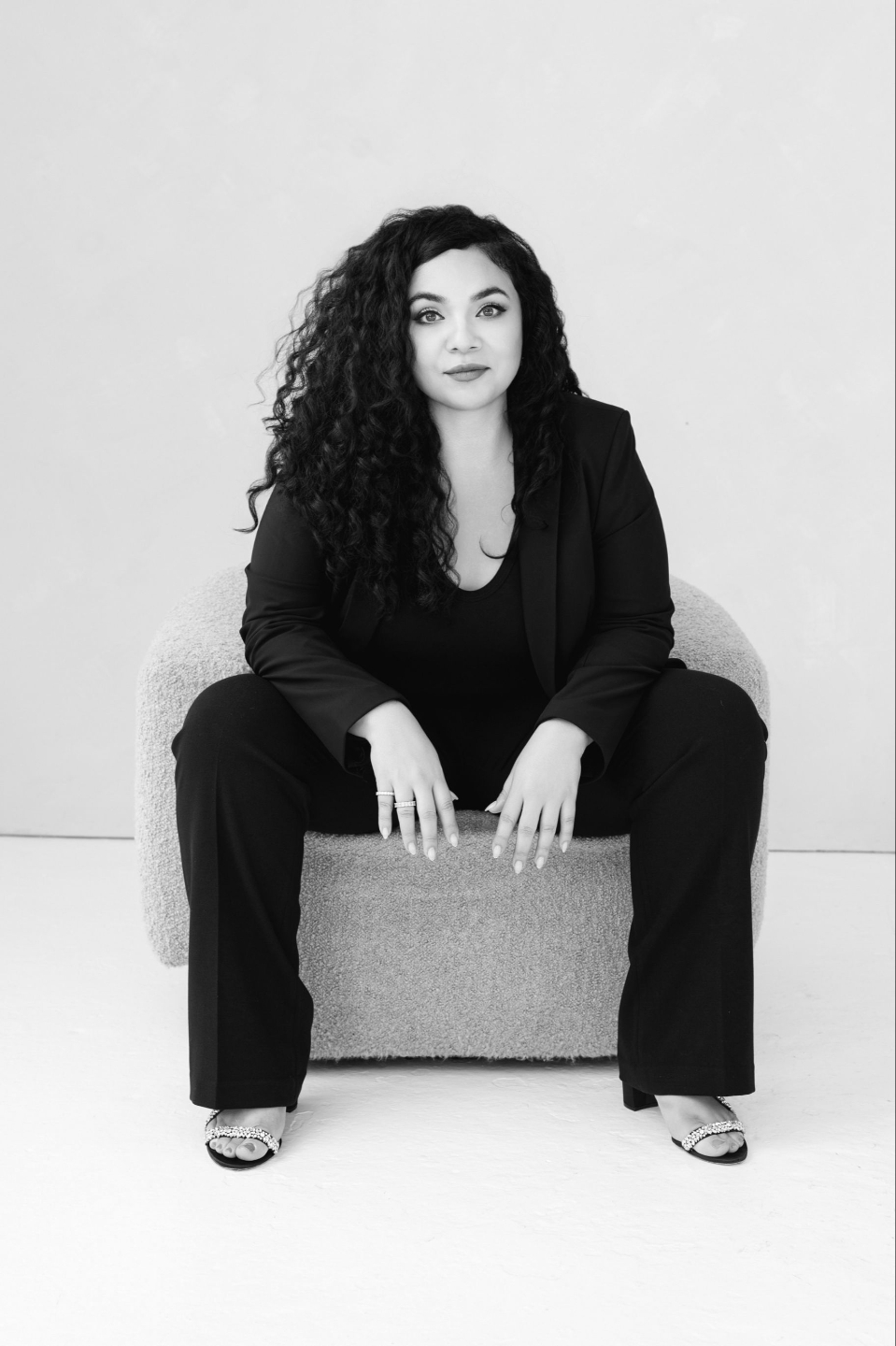 Dunya Daikhi seated in a black suit, black and white portrait