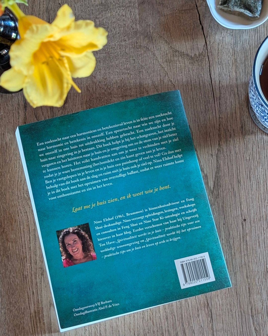 achterkant boek op een houten tafel met afbeelding van Nina Elshof en een quote in gele letters 'Laat me je huis zien, en ik vertel je wie je bent.'