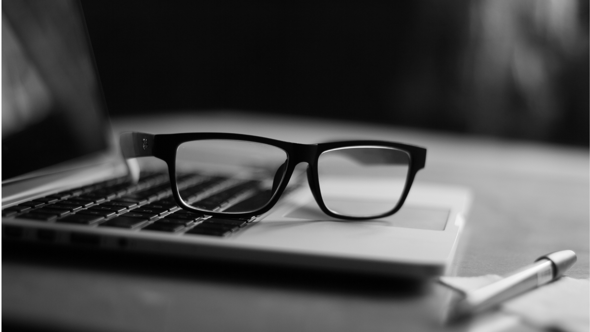 Eyeglasses resting on a laptop beside a pen.