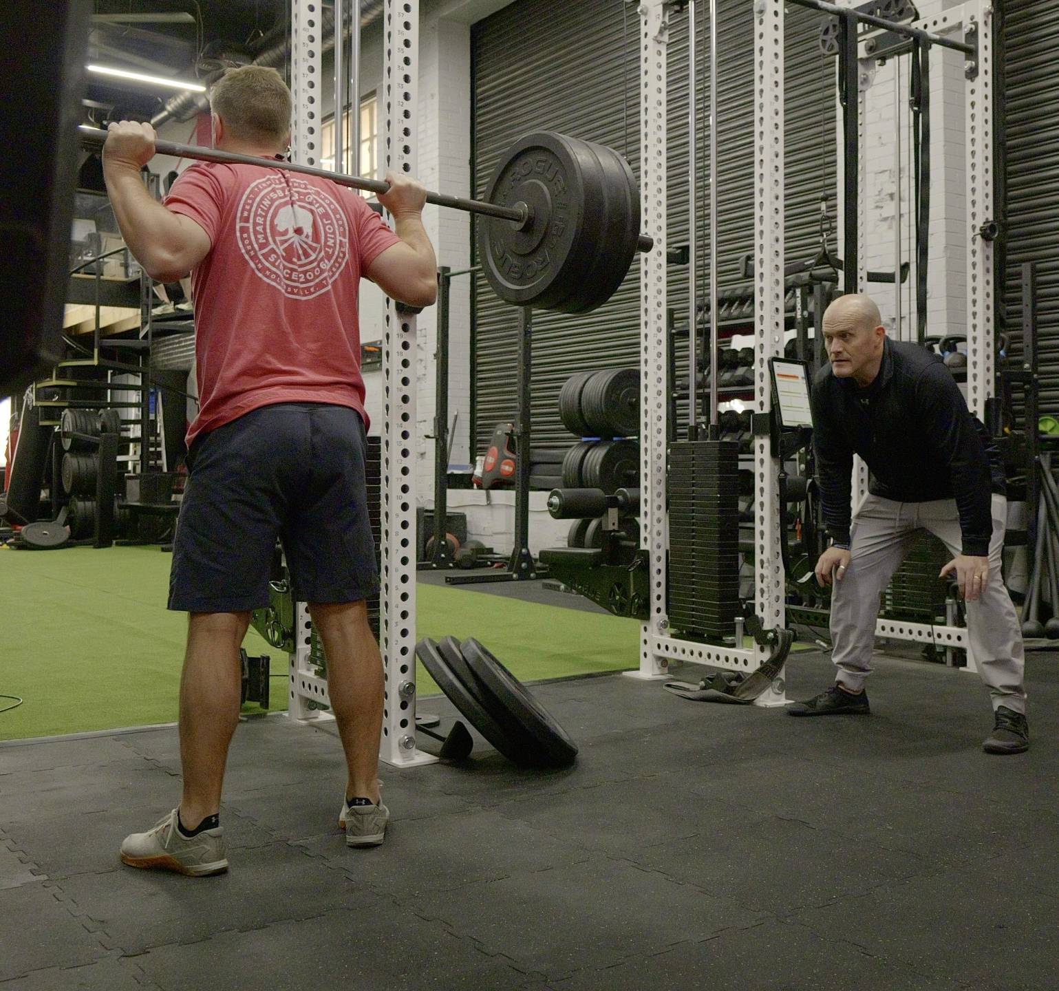 Ben McDonald attentively coaching a client during a barbell squat