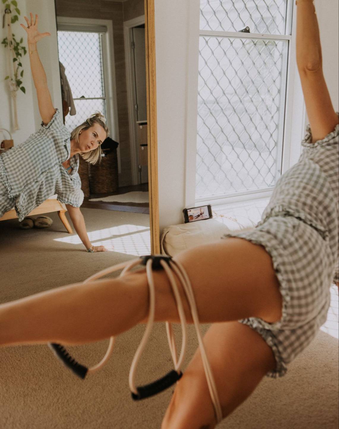 Woman working out in pyjamas in front of a mirror using a pilates reformer exercise band doing a side plank