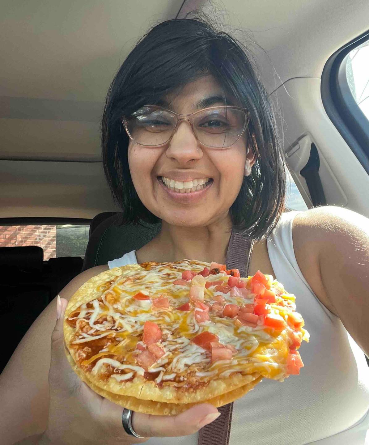 Neha eating a Taco Bell Mexican Pizza in her car