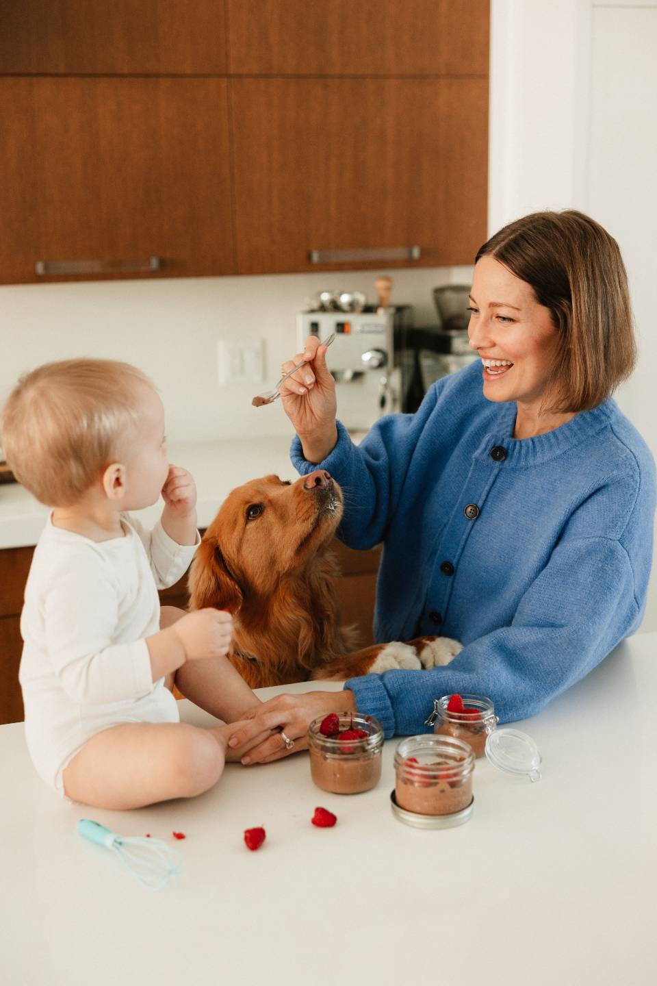 Arianne at the kitchen counter with her baby and her dog, sharing a spoonful of chocolate pudding