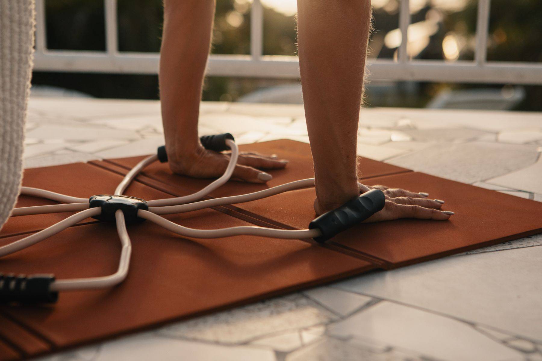 Woman leaning against a door frame looking outside holding a pilates reformer band and a tote bag.