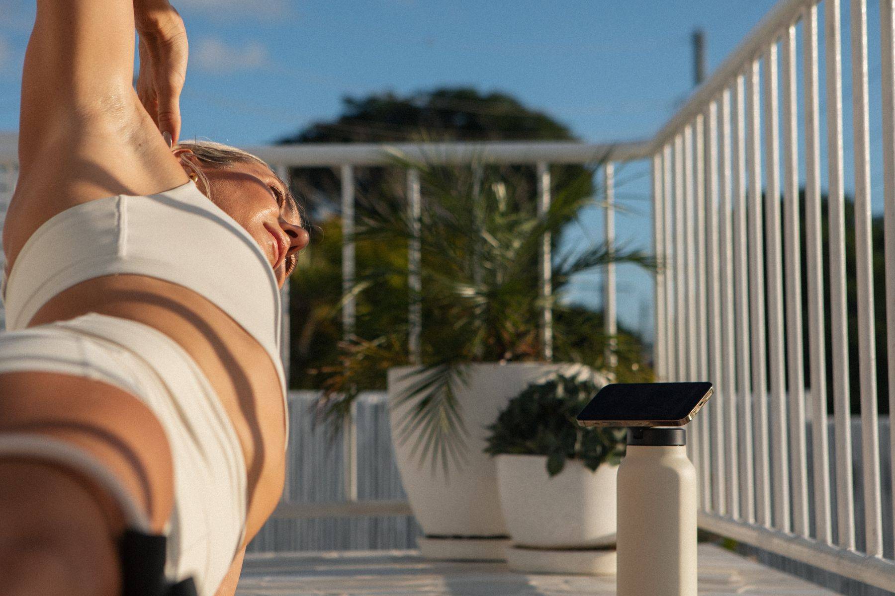 Woman leaning against a door frame looking outside holding a pilates reformer band and a tote bag.