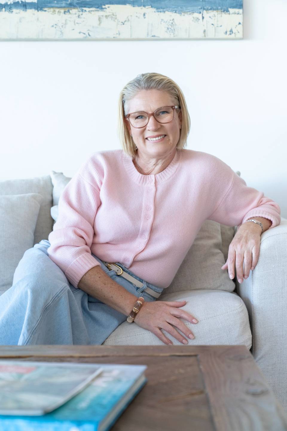 Erin Davis smiling on a sofa in a pink cardigan, photographed at the Dudley shoot