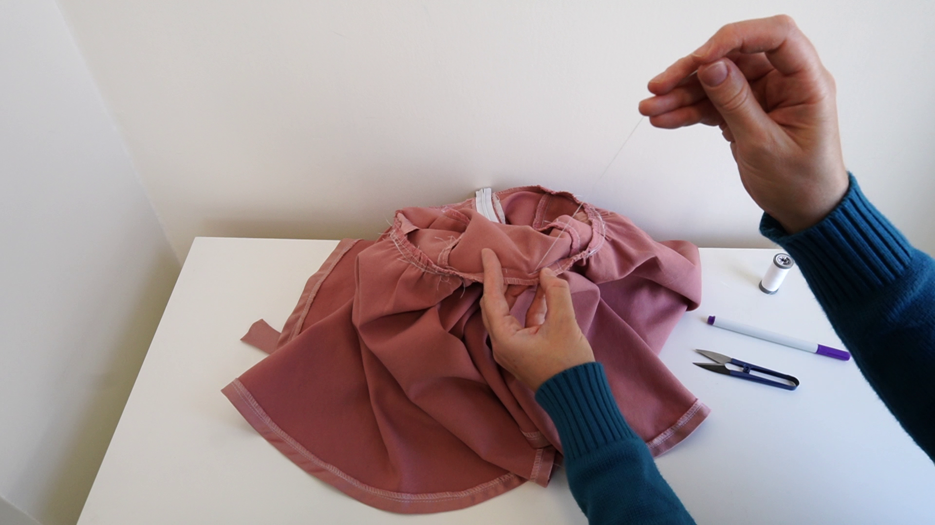 Hands stitching pink fabric with a needle and thread