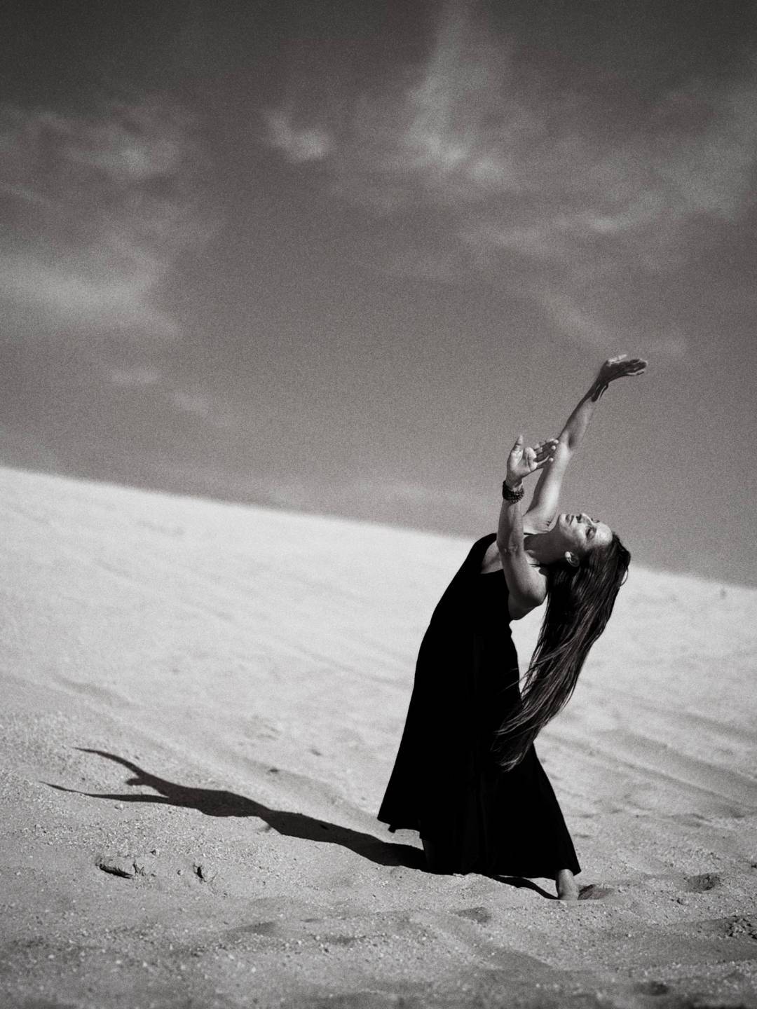 Réka Fodor seated in the sand in a white dress with her arms raised