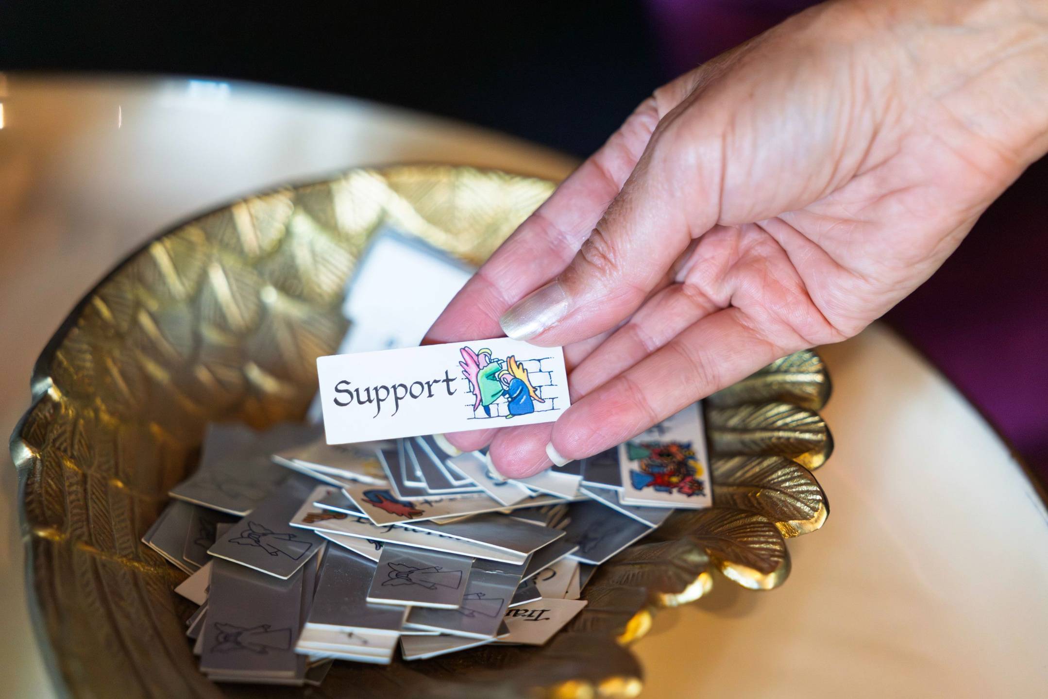 A hand drawing an angel card that reads Support from a gold bowl