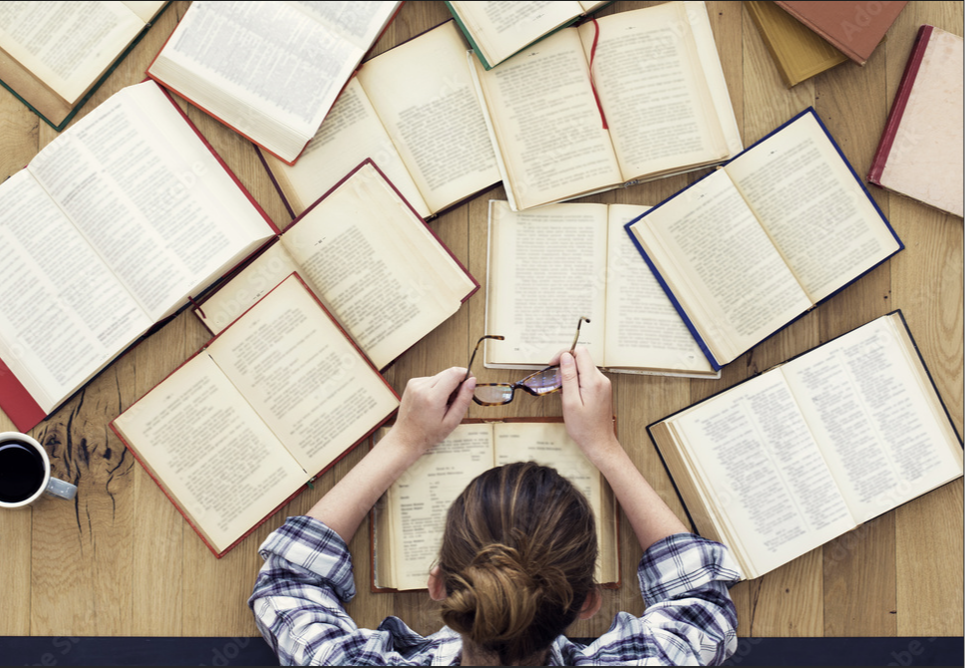 An aerial view of a white woman studying with lots of books spread out open in front of her.