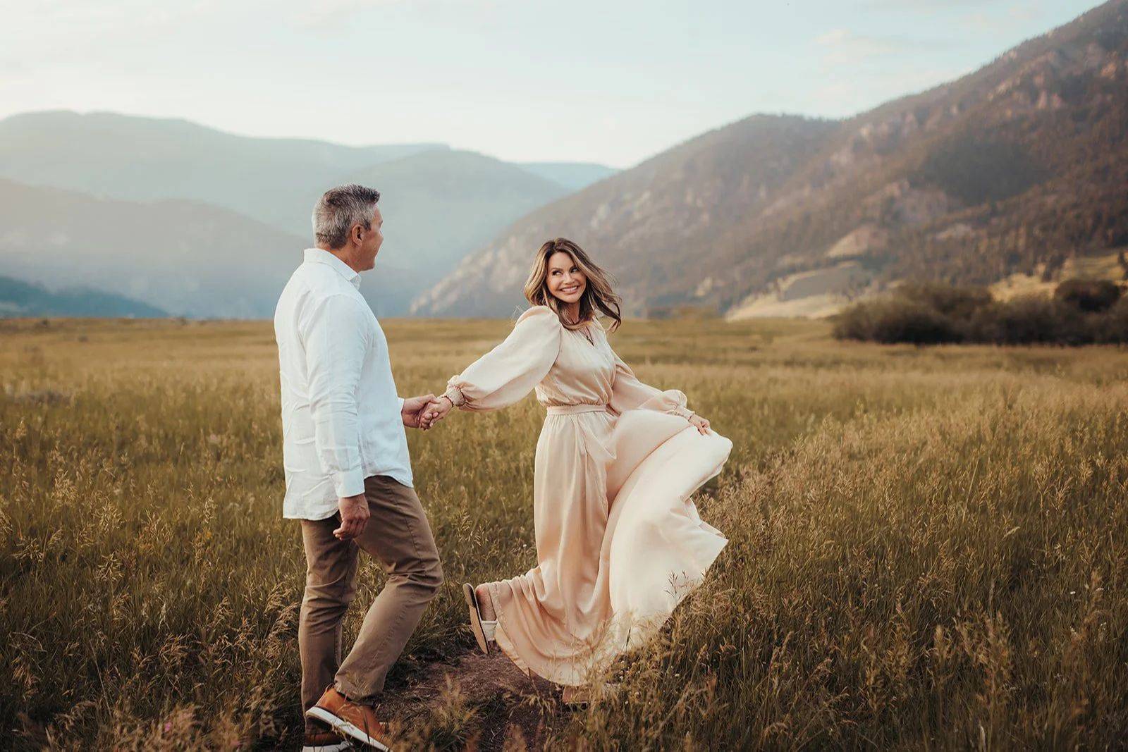 A couple dancing hand in hand through a mountain meadow