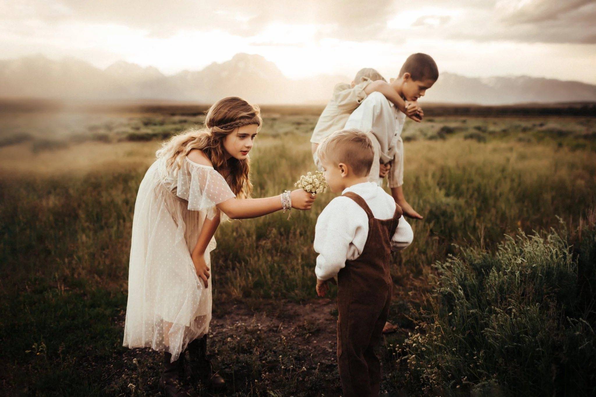A girl offering wildflowers to her little brother in a golden meadow