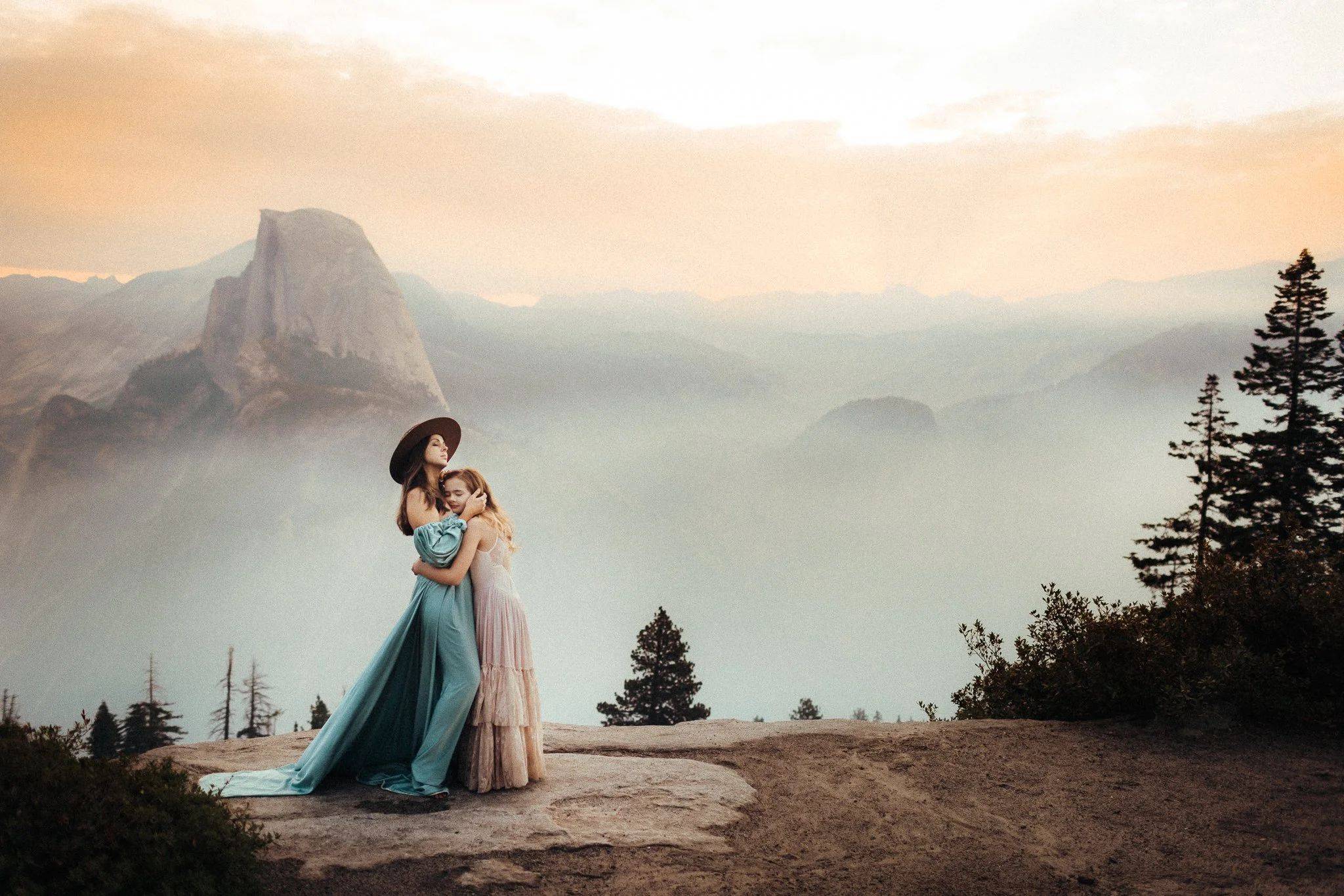 A mother and daughter on a rocky overlook above a misty mountain valley