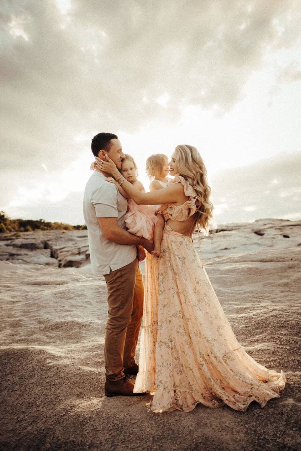 Parents holding their two little girls on the rocks at sunset