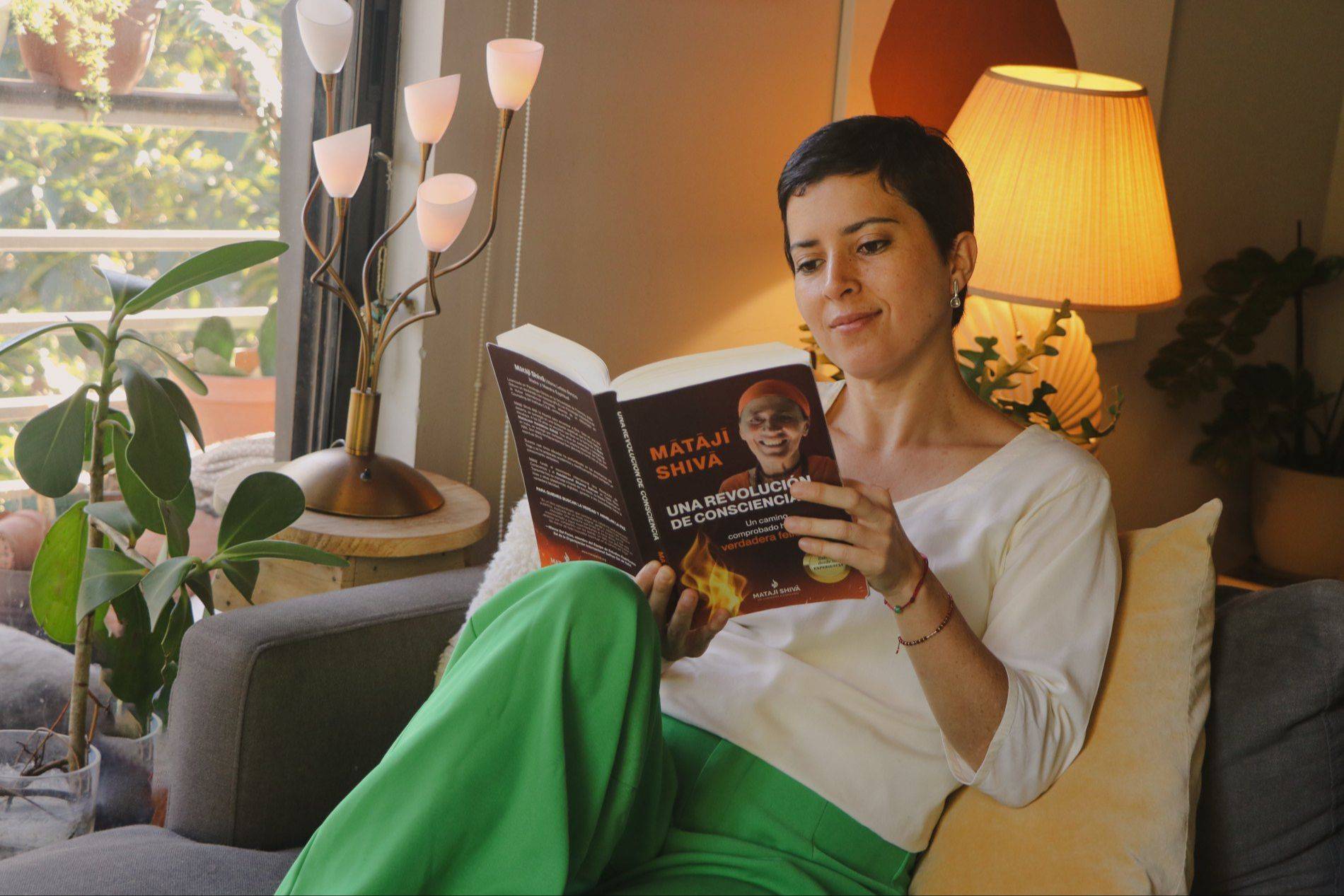 Una mujer lee el libro en un sillón junto a una lámpara encendida