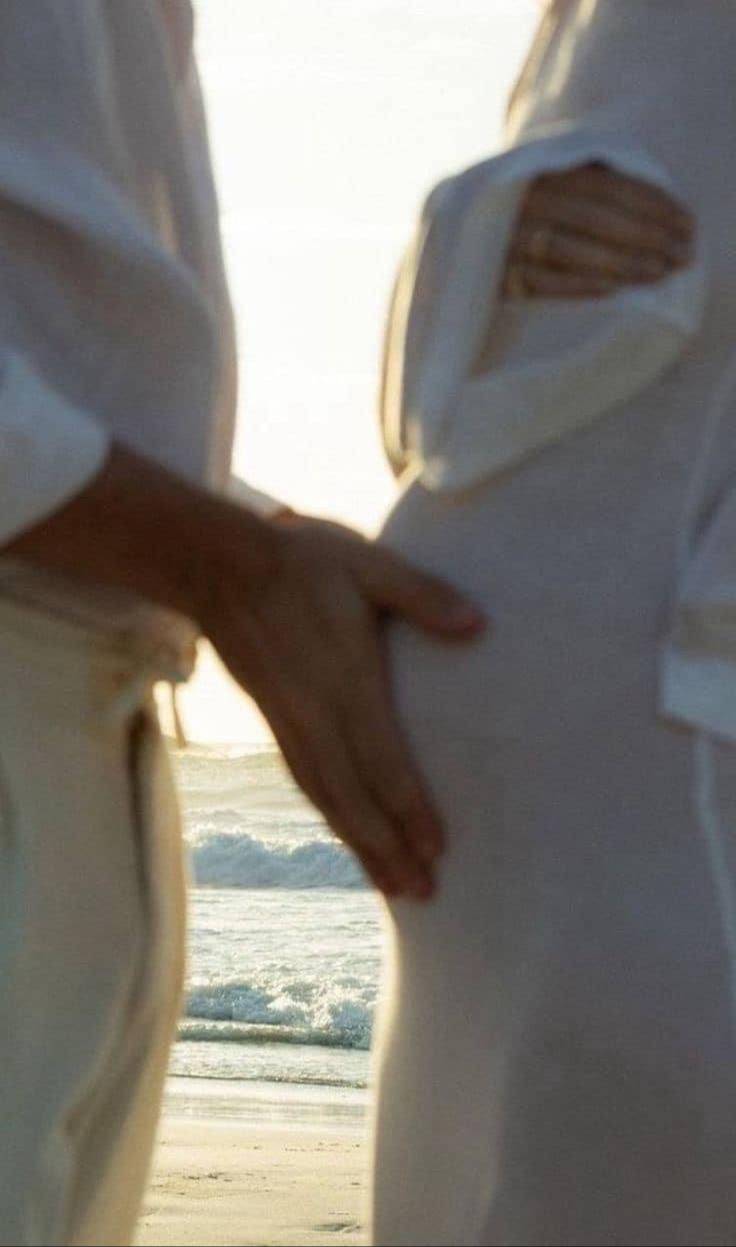 A couple on a beach, one hand resting on a pregnant belly