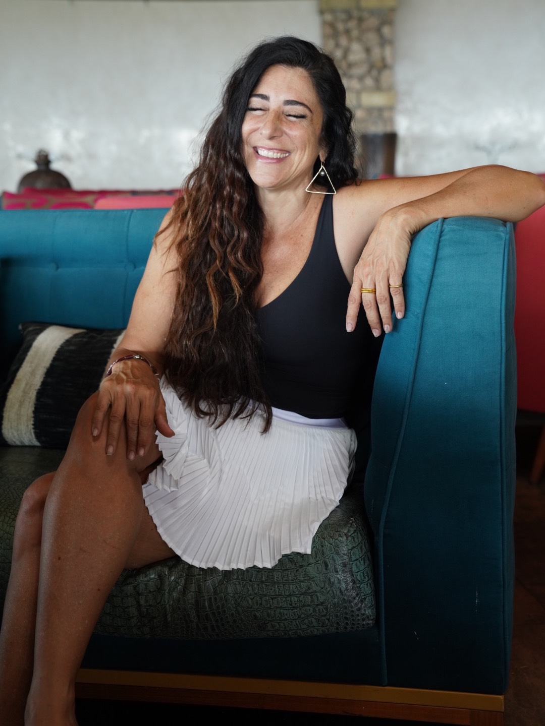Dina smiling with her eyes closed, relaxed on a turquoise sofa.