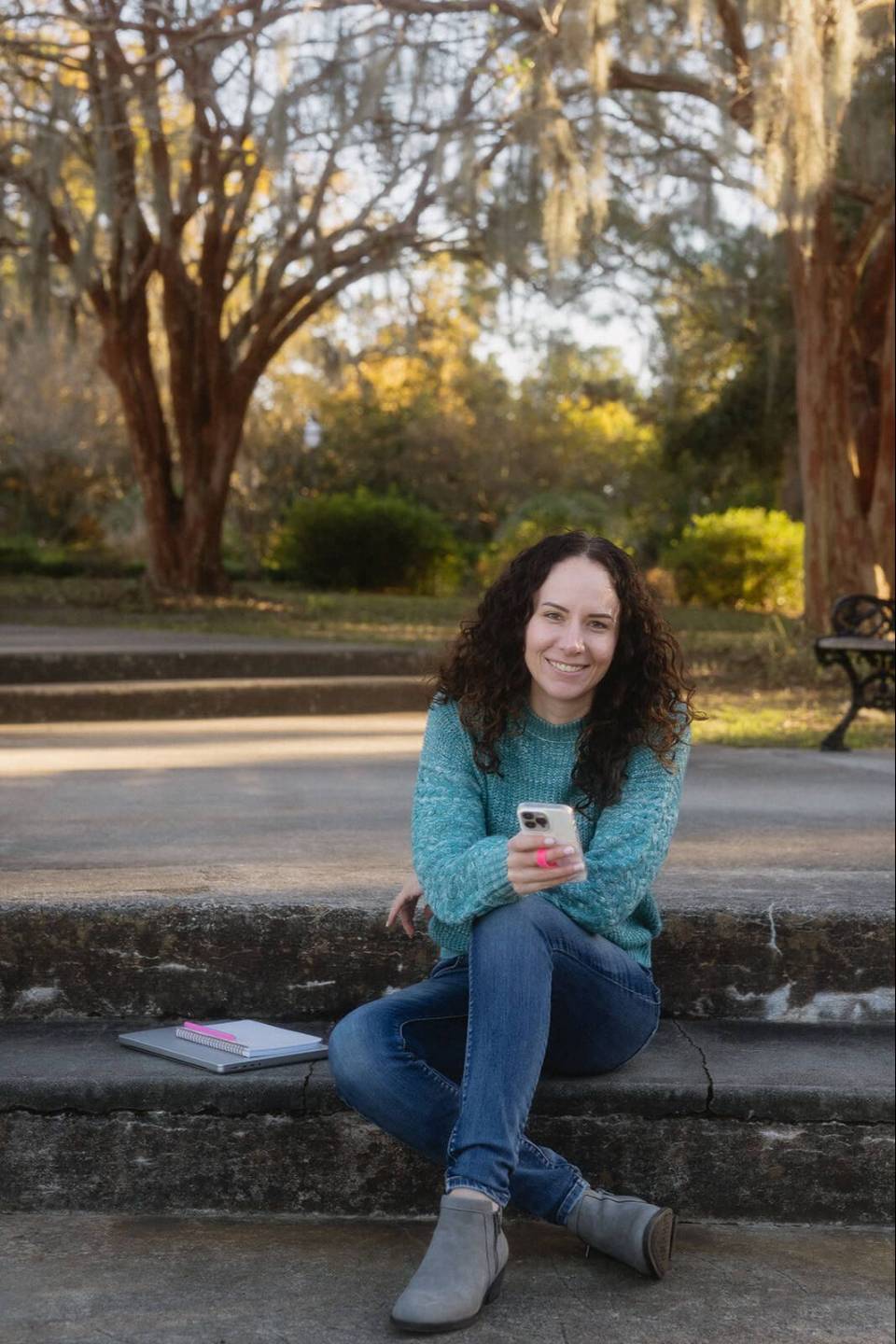 Krista sitting on stone steps outdoors, smiling, holding her phone
