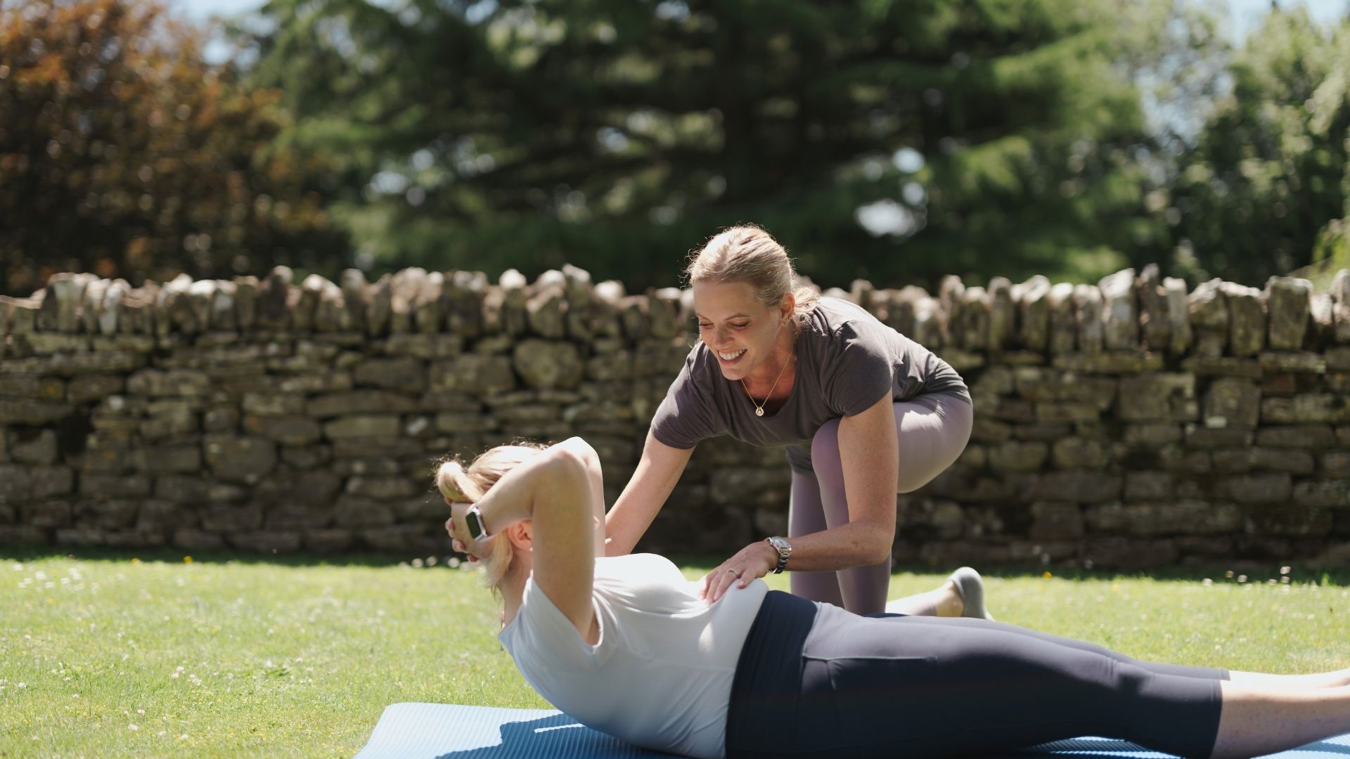 Kari Sherman guiding a woman through a Pilates curl up with hands-on coaching and technique support.
