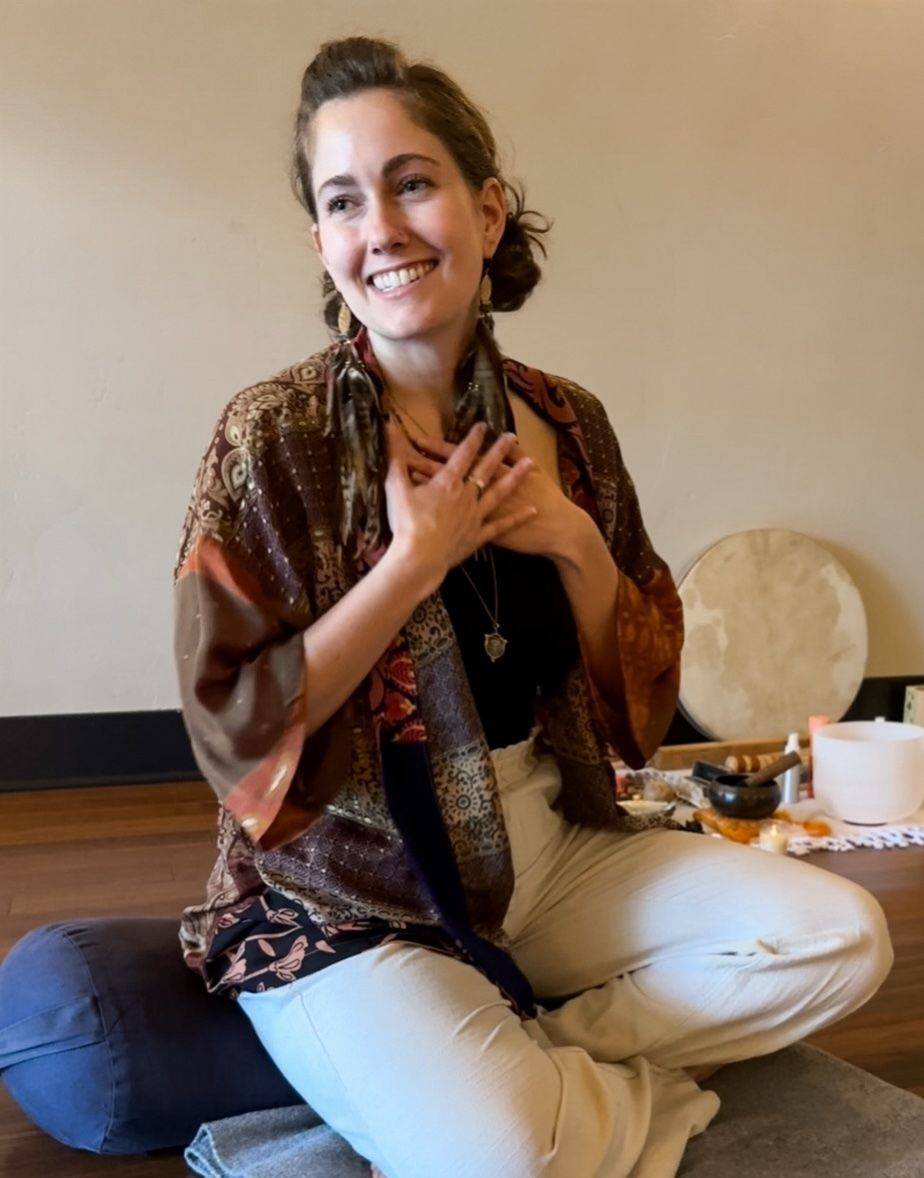 Smiling person with curly brown hair touching face, sitting on white chair