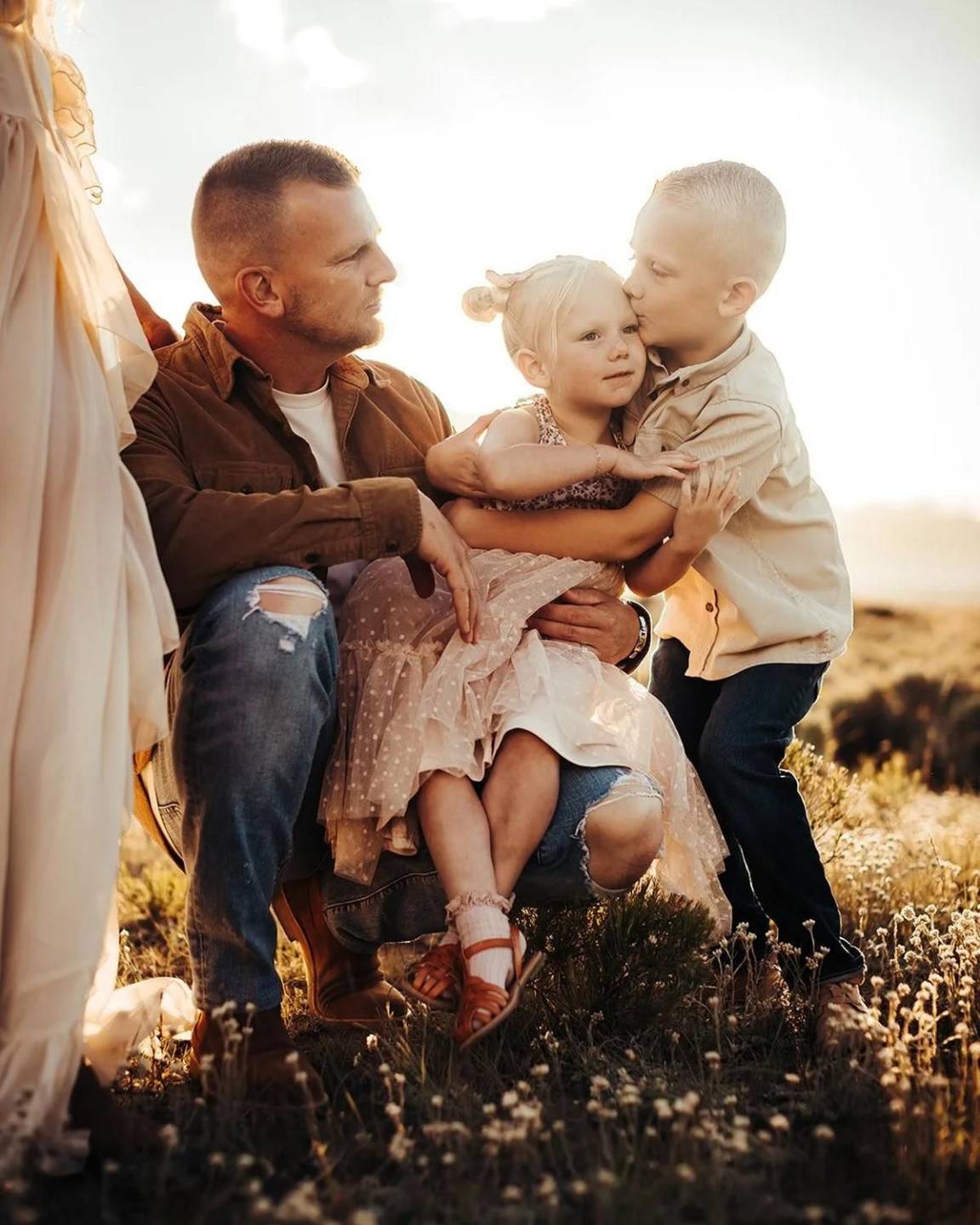 A dad sitting in the wildflowers with his two kids on his lap
