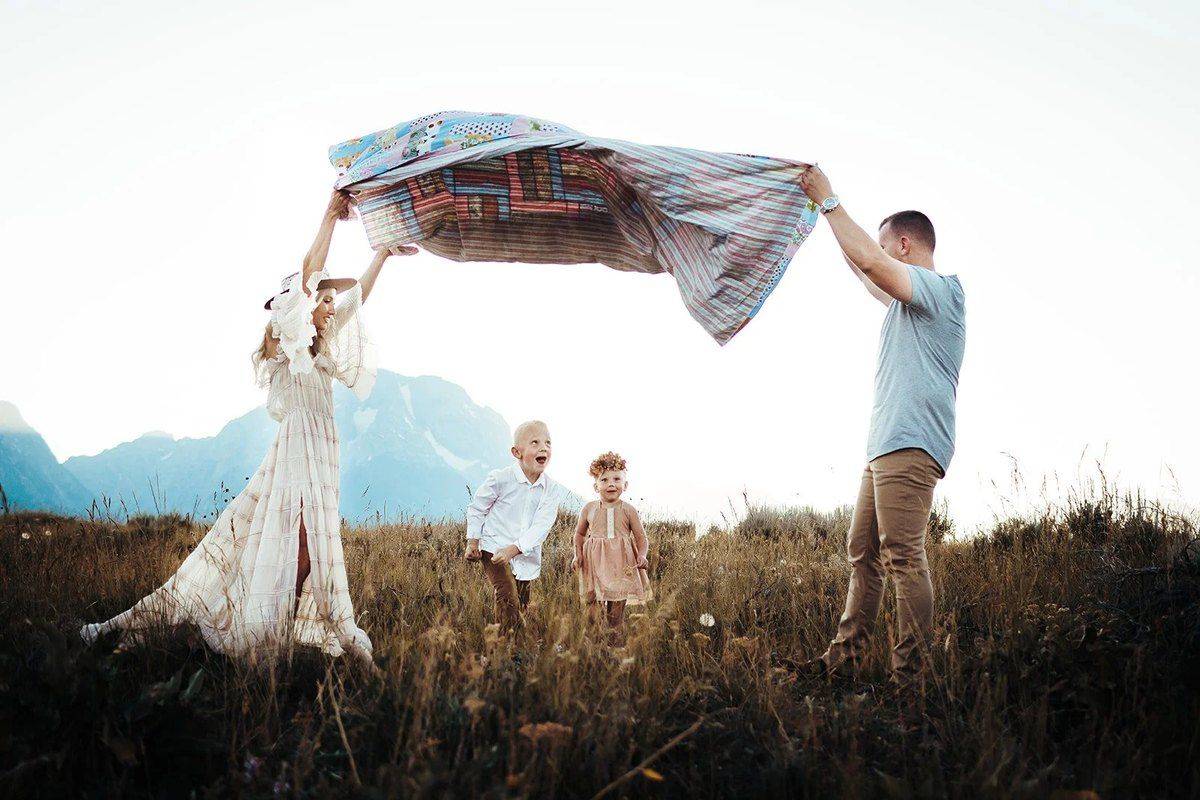 Parents lift a blanket into the wind while their kids run underneath