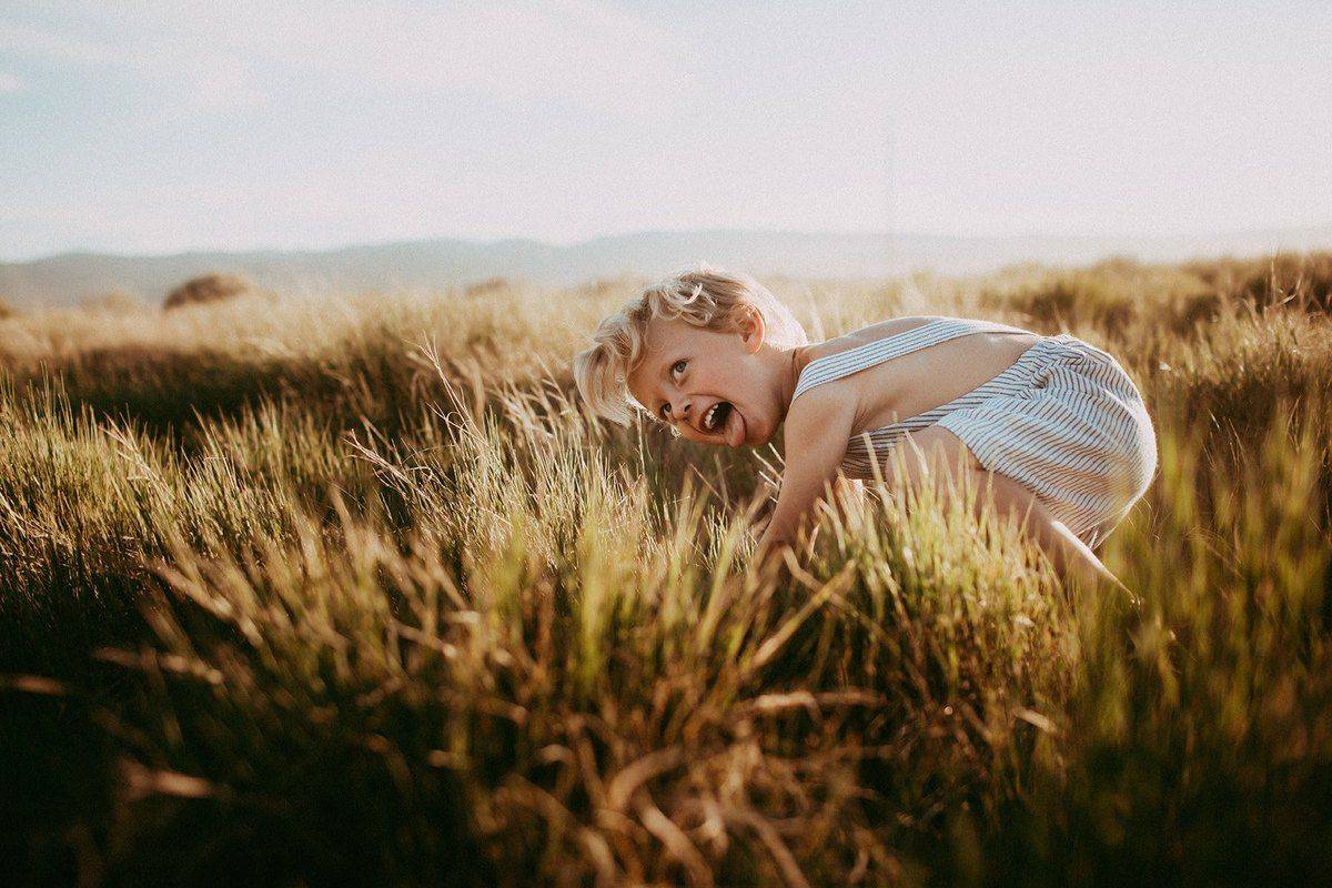A little one lying in the tall grass, mid-laugh