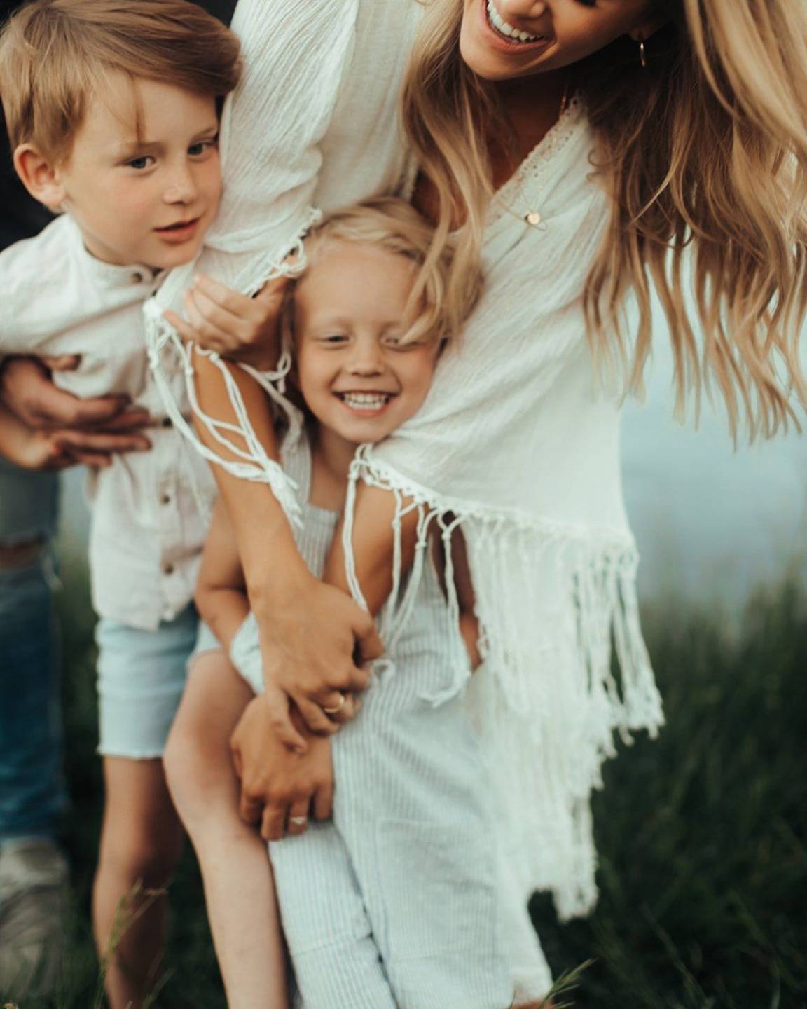 Two kids squeezing their mama in a giggly hug