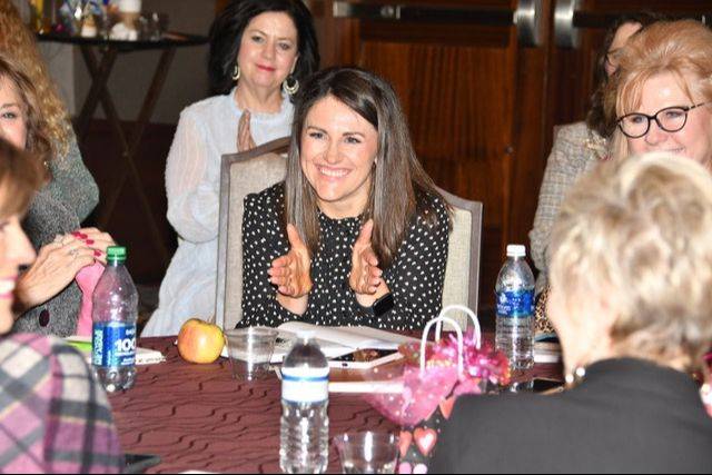 Chelsey smiling and clapping at a table of women during a workshop