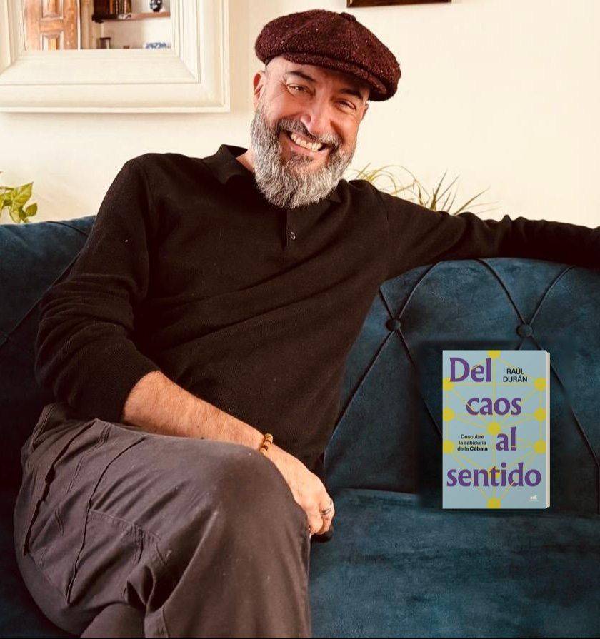Raúl Durán sonriendo en un sofá, junto a su libro «Del caos al sentido»