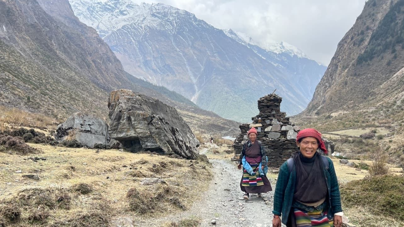 Tibetan villagers walking along a mountain trail in the Himalayas with snow-covered peaks in the background.