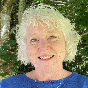 smiling 52 year old woman with wavy mid lenght red hair leaning against a tree